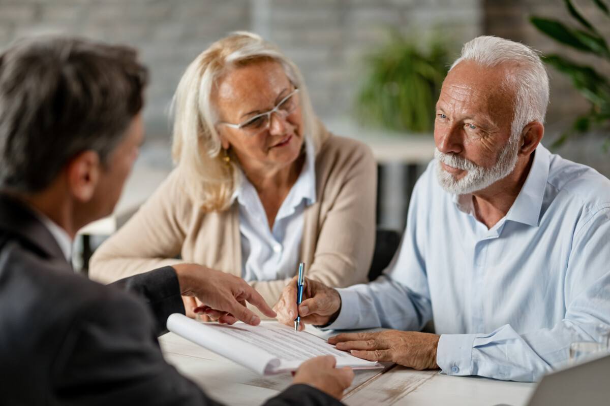 Senior couple signing a contract while having a meeting with ins Mature couple having a meeting with bank manager and signing lease agreement in the office. Focus is mature man.